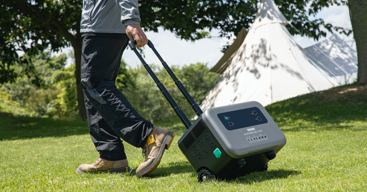 Man walking on grass during day pulling a portable battery generator on the grass behind him using built-in telescoping handle and attached small wheels.