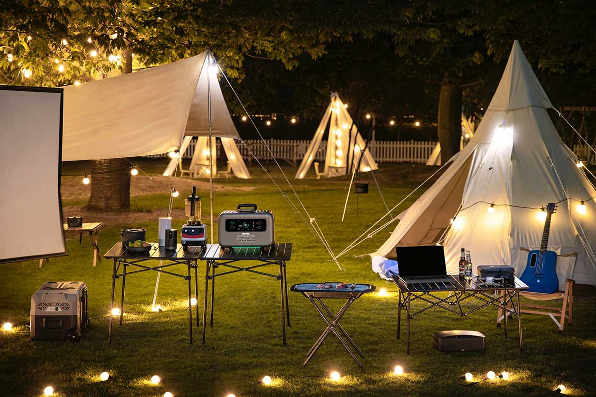Outdoor party setting on grass with tables, chairs and festive teepee tents with electric lights, blender, guitar, laptop, all charged by portable power supply.